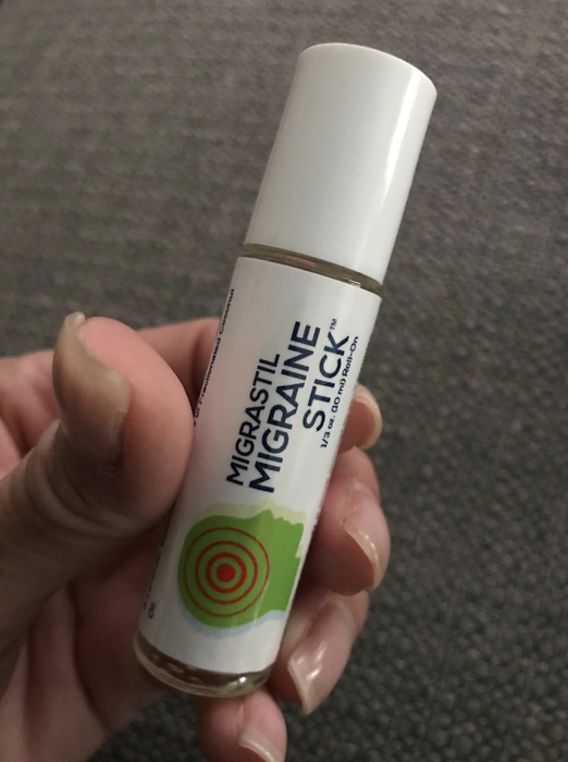 A reviewer's hand grips a migraine stick, which has the convenient shape of a lip balm tube for easy use.