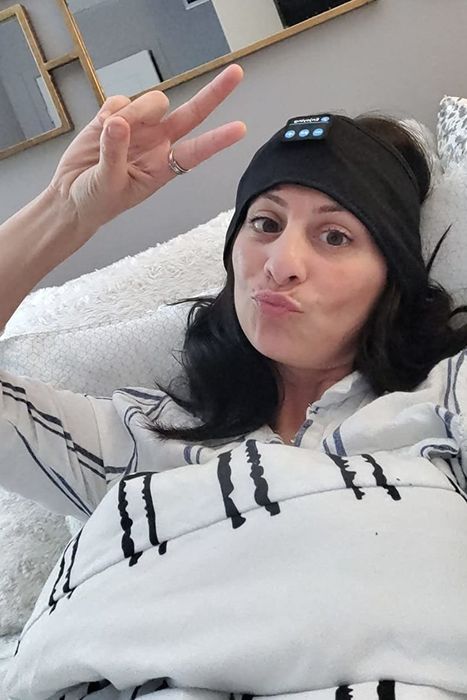 A reviewer in bed wearing a black headband, flashing a peace sign with their right hand
