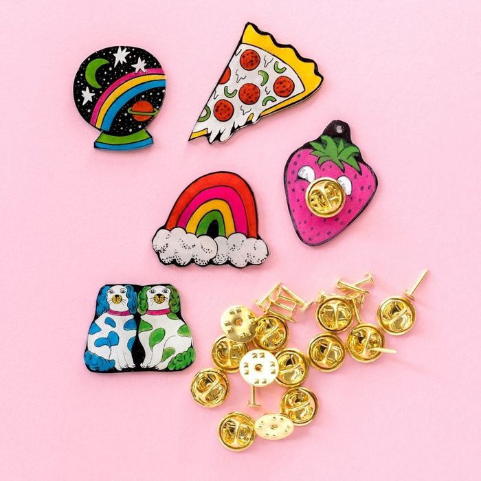 the completed and colored designs of pizza, crystal ball, strawberry, rainbow, and dog, each with gold pin backs