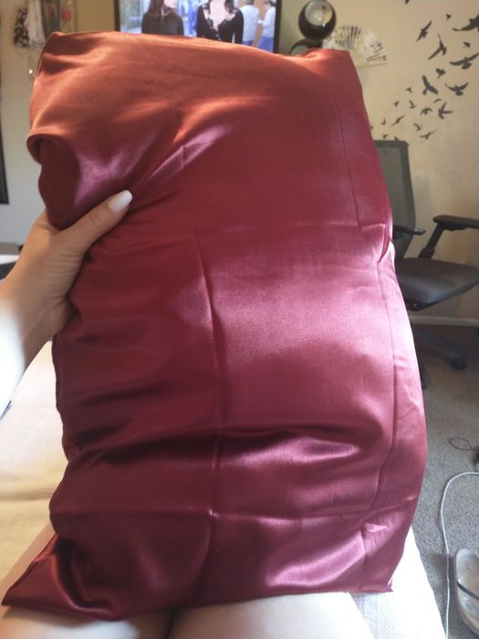 A reviewer holding up a pillow with a burgundy satin pillowcase