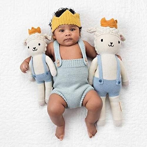 A baby pictured next to two dressed lamb dolls, one large and one small, both adorned with crowns.