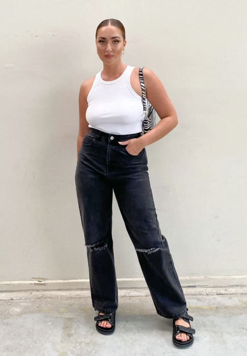 A model rocking black wide-leg jeans with ripped knees, paired with a white tank top.