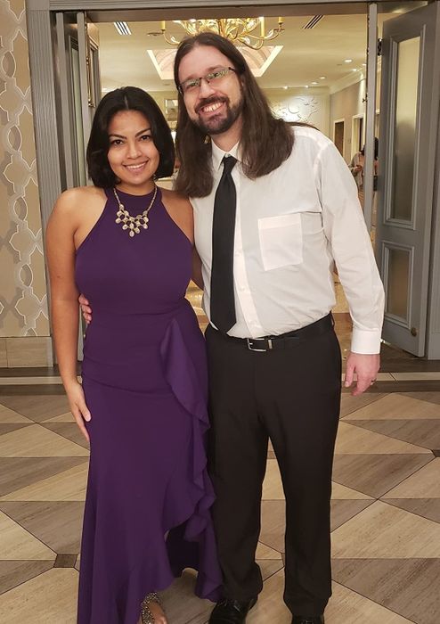 a reviewer wearing the purple dress, standing next to someone in black pants, a white button-up, and a black tie