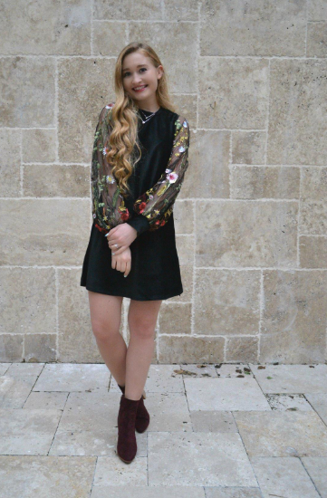 Reviewer modeling the black mid-thigh tunic dress with black mesh sleeves and embroidered floral accents.