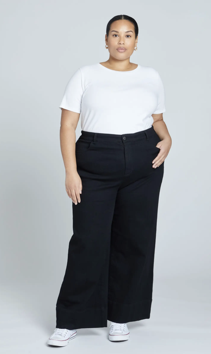 A model in black high-waisted wide-leg jeans, paired with a white t-shirt and sneakers.