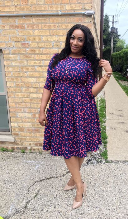 A reviewer wearing the knee-length blue dress adorned with tiny red flowers