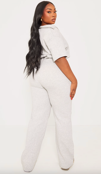 Woman in a casual gray jumpsuit posing with one hand on her hip