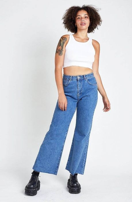 Model wearing raw-hem, wide-leg blue jeans paired with black platform shoes.