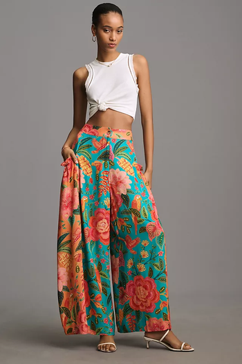 model in a white crop top and floral wide-leg pants, posing with one hand on her hip