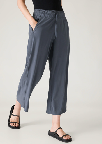 Person styling casual elastic-waist trousers with black sandals, standing with a hand in their pocket for a laid-back look