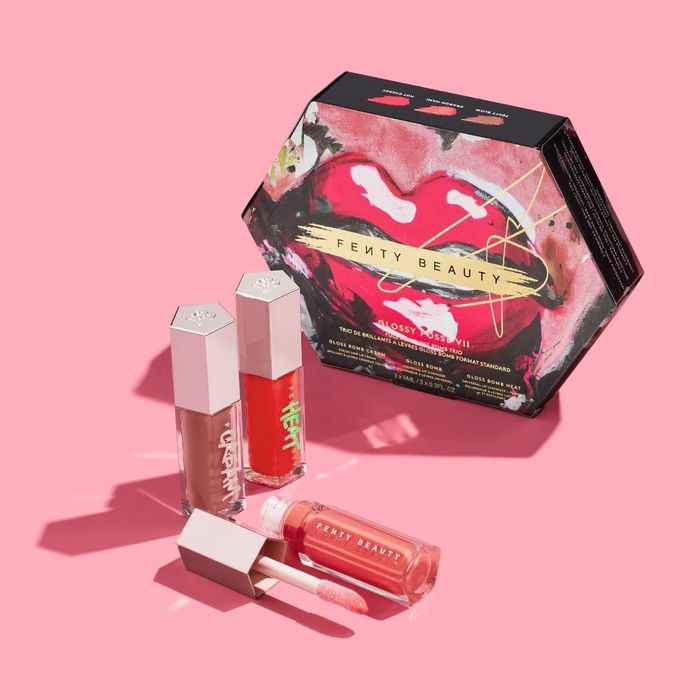 The Fenty Beauty Glossy Posse set showcasing three lip glosses with decorative packaging on a pink backdrop