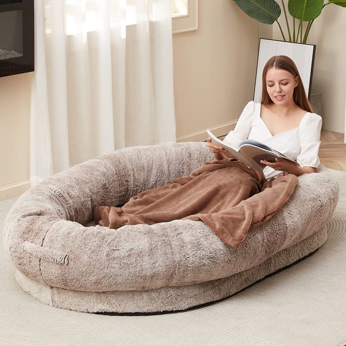 A model lounging in a beige oval-rimmed bed placed on the floor