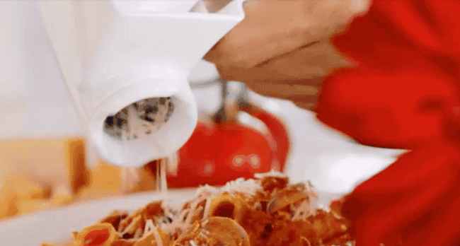 A gif of a hand turning the grater, showering Parmesan over a plate of pasta