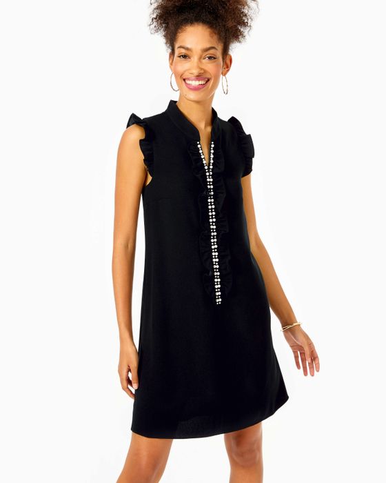 A model wearing the sleeveless dress, adorned with pearls down the front and ruffled shoulders