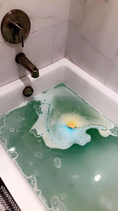 A bathtub scene showcasing a colorful bath bomb dissolving, creating vivid swirls in the water, as featured in a shopping article.