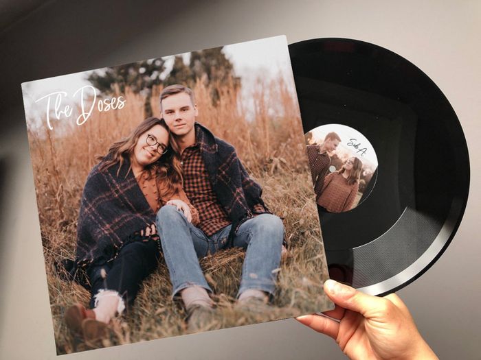 A hand holding a vinyl record featuring a personalized photo label next to its album cover