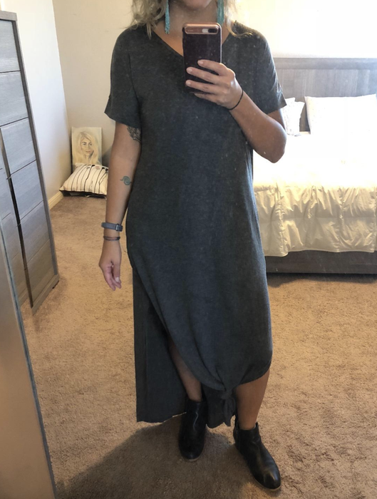 The reviewer is wearing a gray dress knotted in the front, paired with blue earrings and black booties.