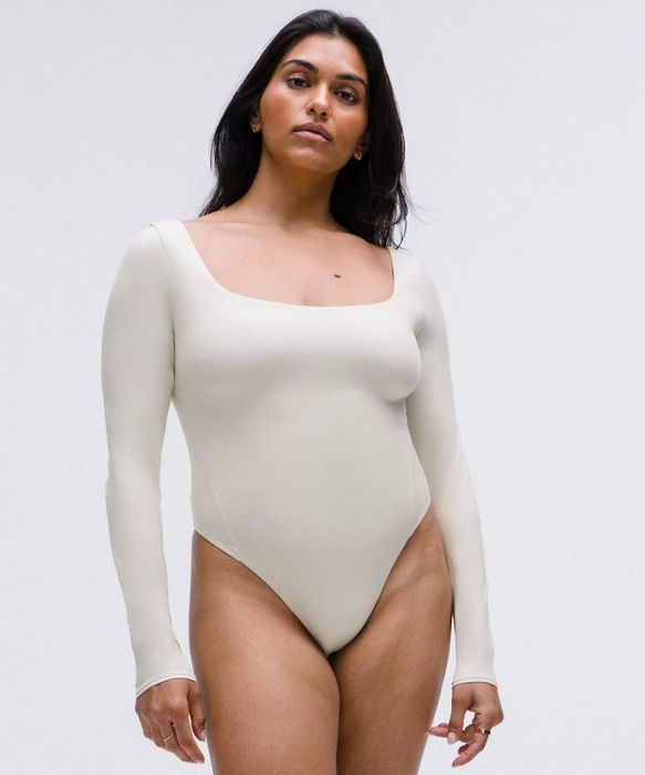 A woman is wearing a long-sleeve bodysuit with a square neckline.