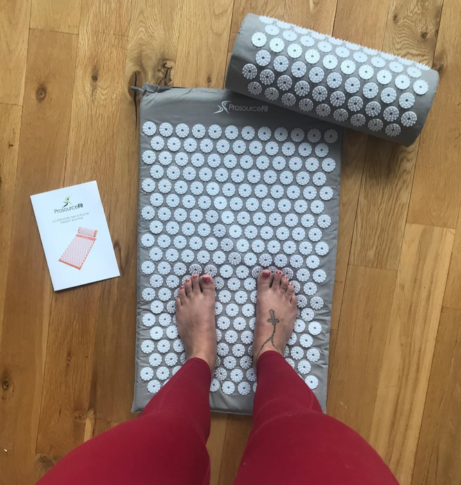 A reviewer standing on the acupressure mat, dressed in gray