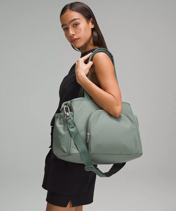 A model elegantly poses in a chic black ensemble, carrying a large, modern handbag with multiple compartments for both style and practicality.
