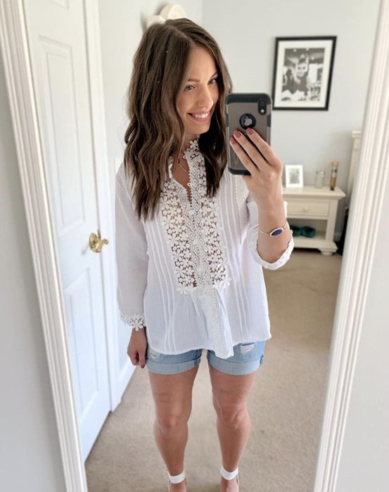 A person styled in a white floral-detailed blouse paired with denim shorts