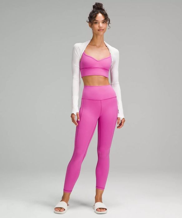 A woman showcases a chic activewear ensemble featuring a pink sports bra, matching leggings, a white long-sleeve open-front top, and white slip-on sandals