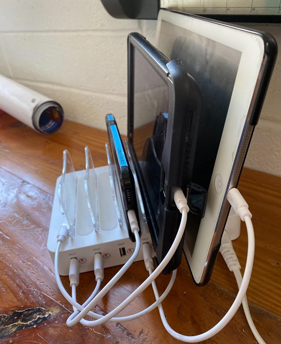 A reviewer's photo of the charging station powering a phone and two tablets, with additional slots still available