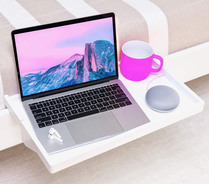 a white shelf securely attached to a bed frame, holding a mug, a speaker, and a laptop