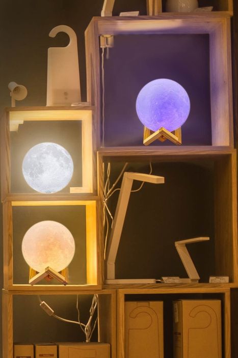 Three moon lamps glowing in different colors, placed on a shelving unit