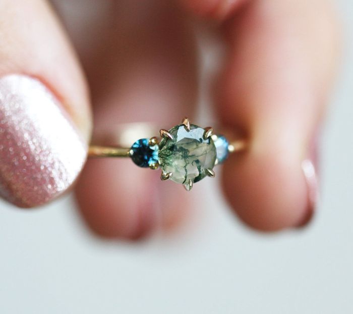 a hand holding the green and blue ring secured by gold prongs