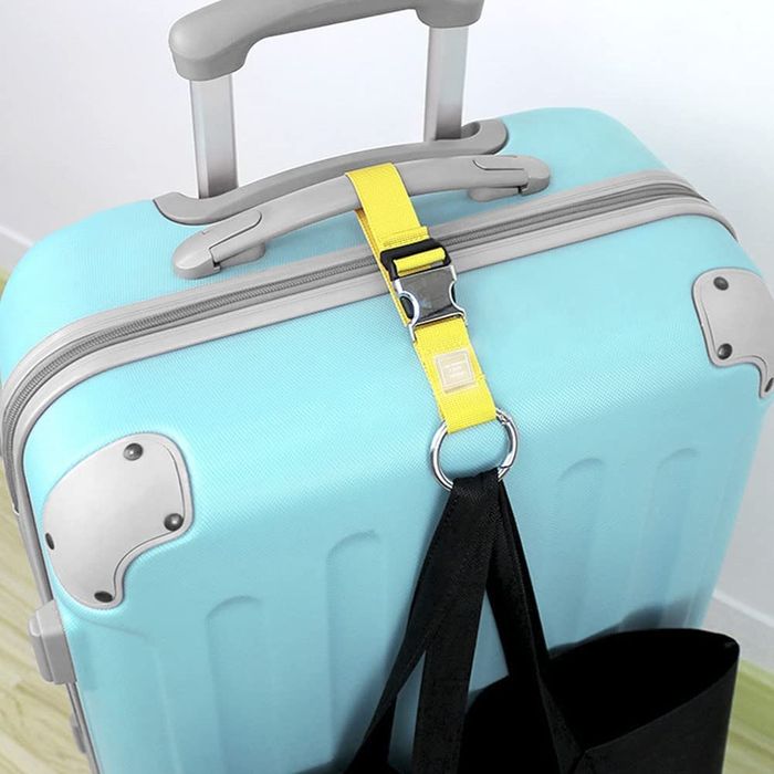 A yellow luggage strap fastened to a rolling suitcase, holding a tote bag securely.