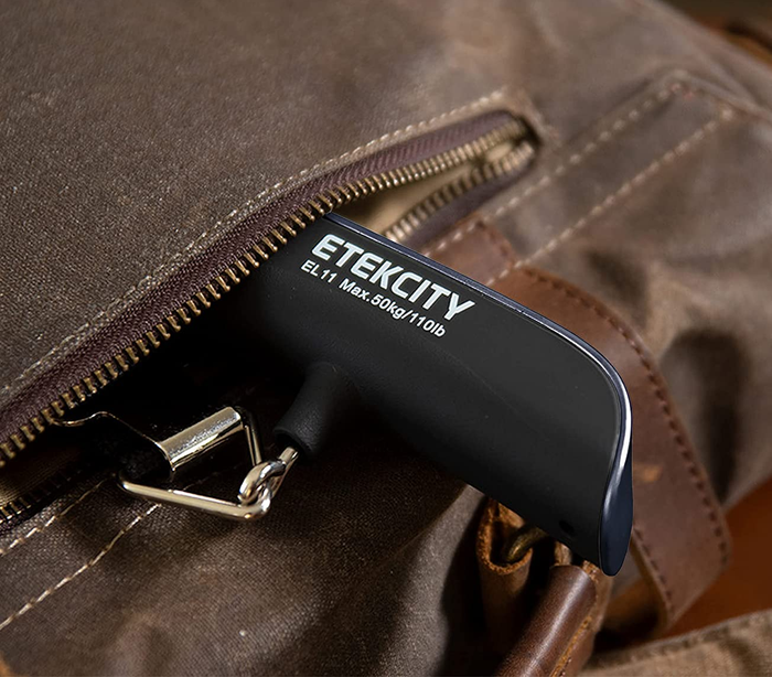 A black luggage scale peeking out from the pocket of a travel bag