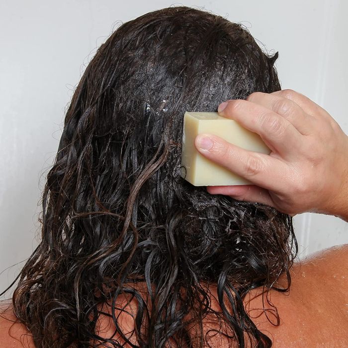 A model washing their hair using a shampoo bar, shown from the back