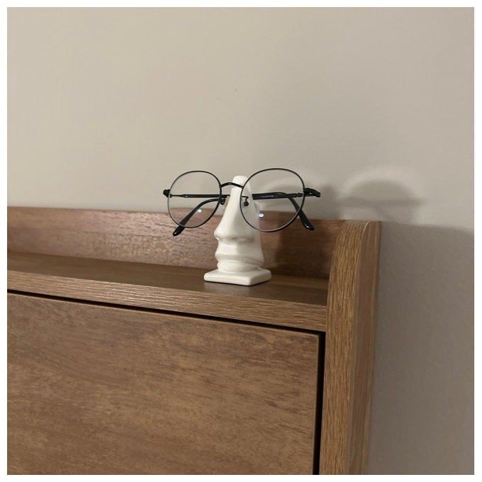 Eyeglasses placed on a small white bust atop a wooden shelf, creating an elegant display.