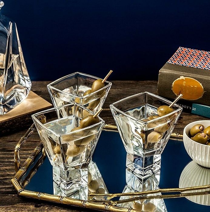 Martini glasses with olives resting on a mirrored tray beside a stack of books.