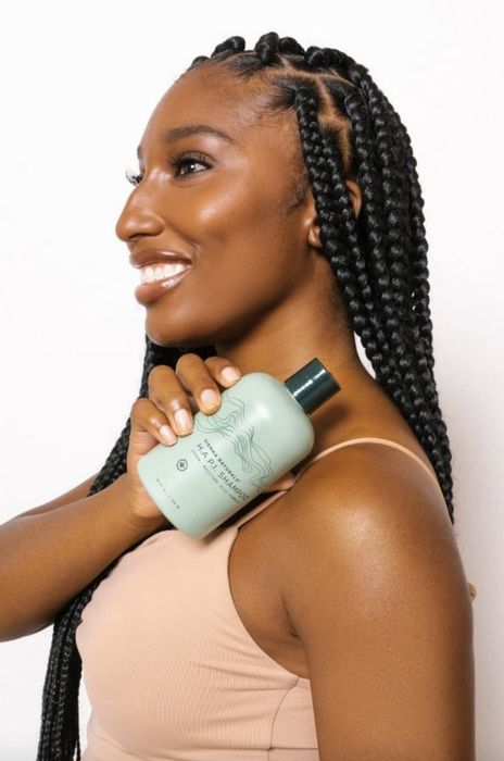 A person with braids holding a bottle of shampoo