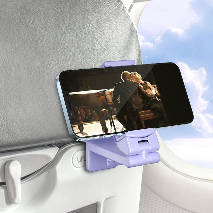 A purple phone mount securely attached to an airplane seat-back tray, holding a phone displaying a movie