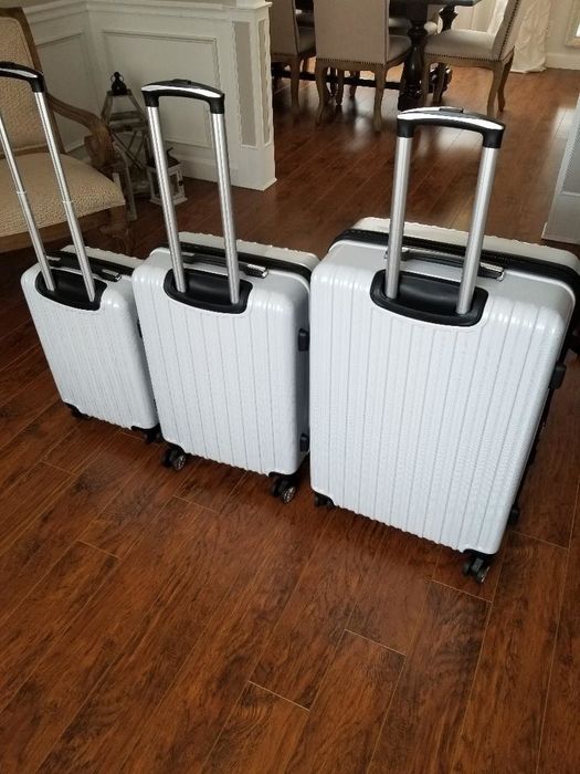 The reviewer displays their three white suitcases of varying sizes, each with the handles extended, showcasing their easy maneuverability.