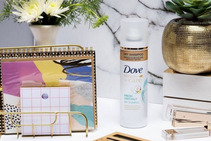 A can of dry shampoo alongside notebooks and flowers
