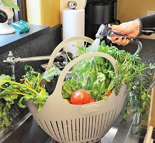 A person washing fresh vegetables in a colander at the kitchen sink