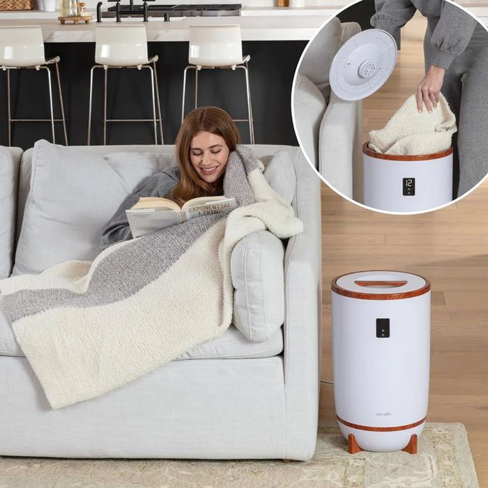 A person unwinding with a book wrapped in a cozy blanket, positioned next to a portable space heater.