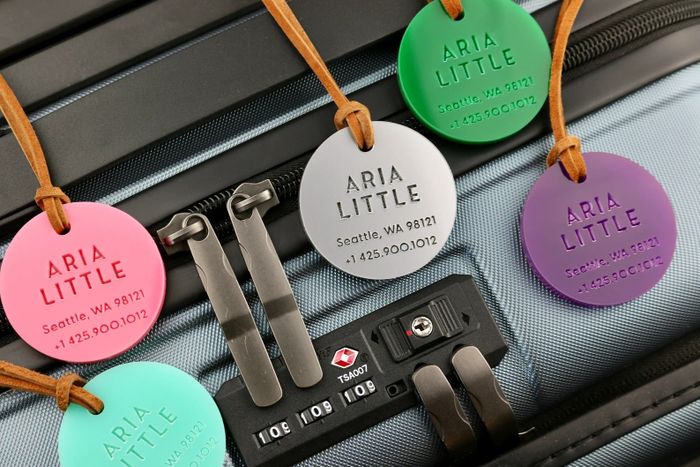 A collection of round, personalized luggage tags in various colors displayed on a suitcase.
