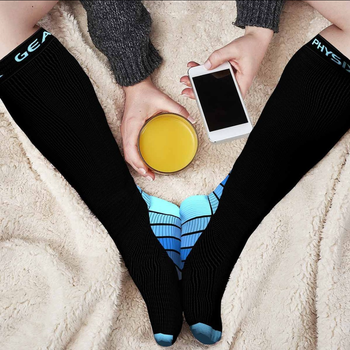 A model wearing blue-and-black compression socks, casually using their phone and holding a glass of juice.