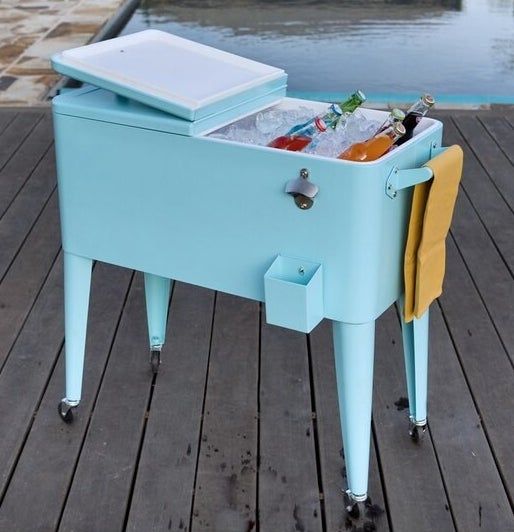 A light blue cooler with caster wheels, the lid open to reveal ice and refreshing beverages inside.