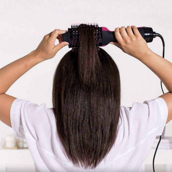 A person styling their hair with a heated brush and dryer