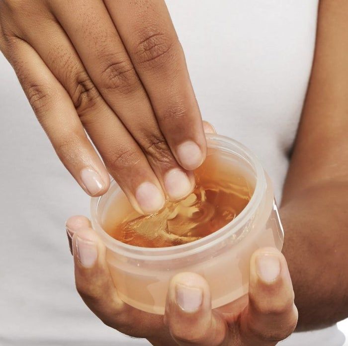 A person dipping their finger into a jar of edge control gel