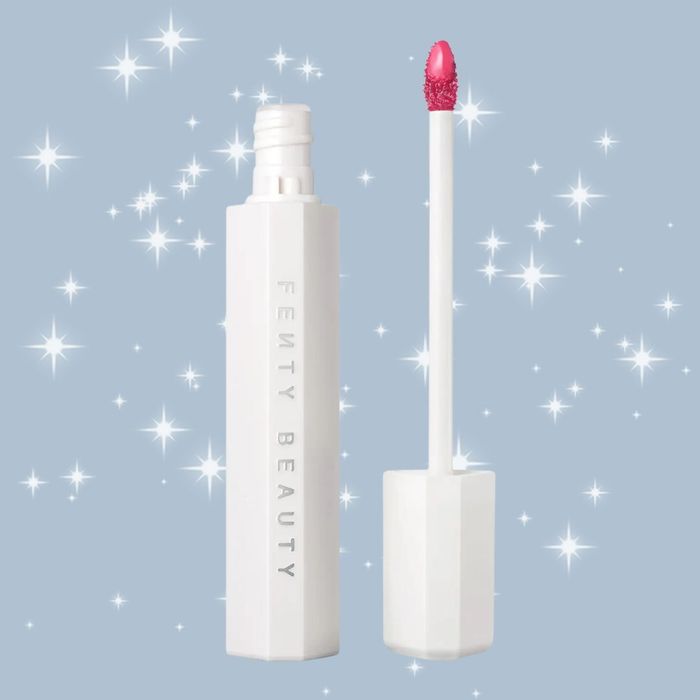 An open Fenty Beauty lip gloss tube with a pink gloss applicator, set against a glittering starry background