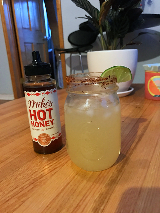 The honey bottle placed beside a yellow drink in a mason jar.