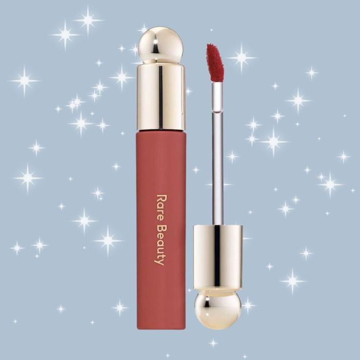 A Rare Beauty lipstick and applicator displayed against a sparkling, star-filled background