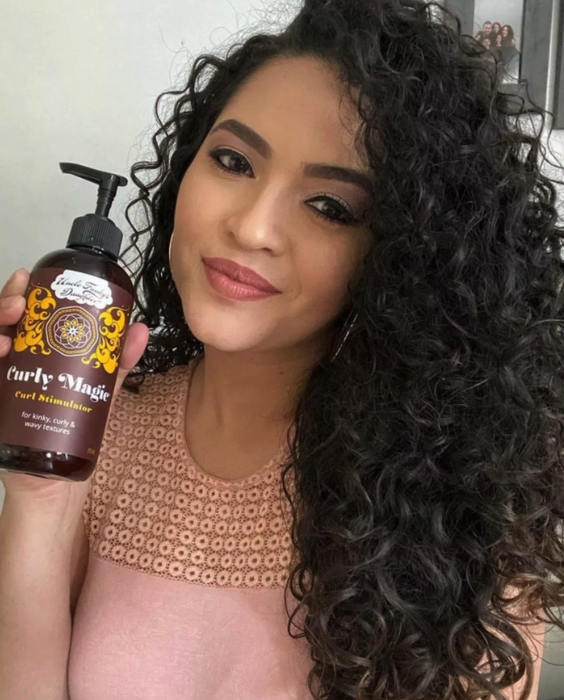 A model with long curly hair holds the bottle of hair product, showcasing the perfect styling solution.